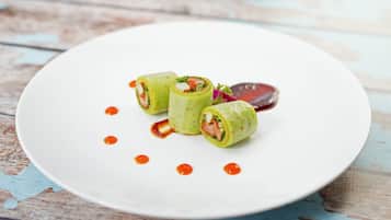 Une assiette blanche sur laquelle sont disposés trois amuse-gueules roulés et une tranche de betterave, le tout posé sur une table en bois rustique.