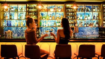 A bar with two patrons seated at the bar, a wooden ceiling, and shelves stocked with bottles.