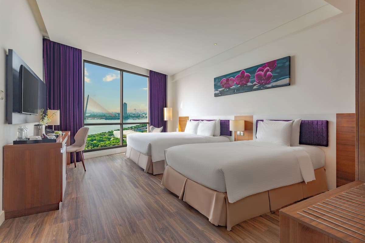 Habitación de hotel con dos camas, un escritorio, un televisor y un ventanal con vistas a la ciudad.
