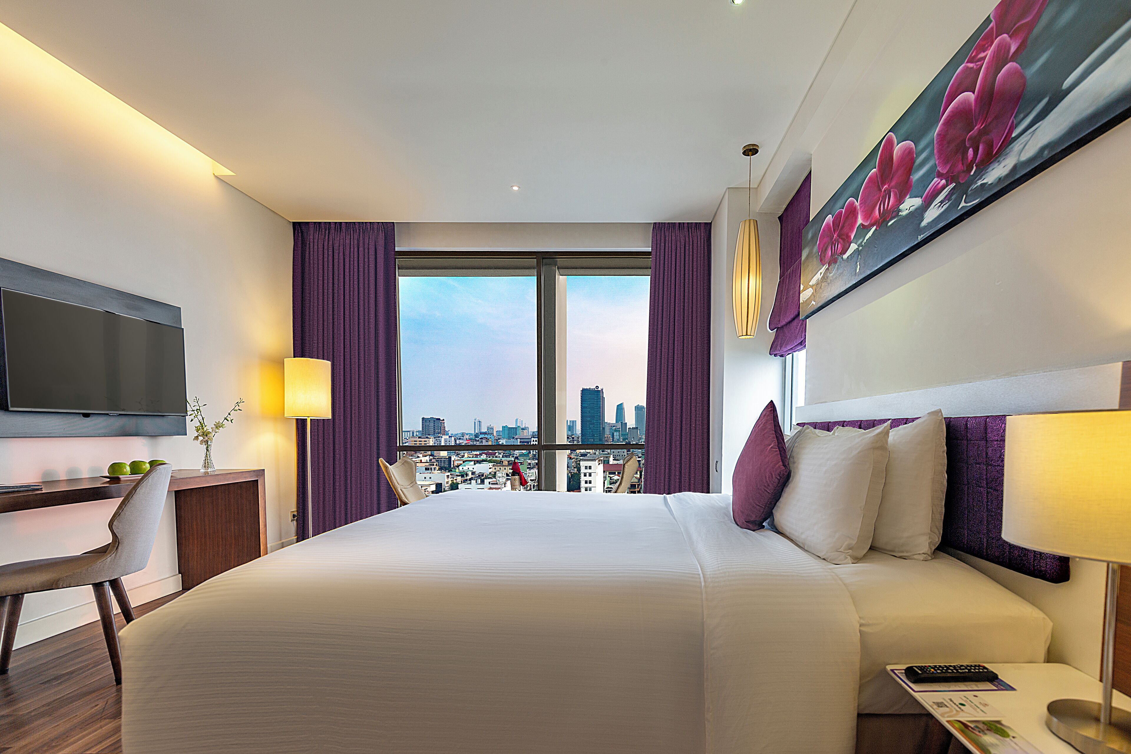 A modern hotel room with a large bed, a desk, a chair, a television, and a city view.