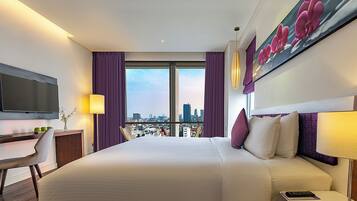 A modern hotel room with a large bed, a desk, a chair, a television, and a city view.