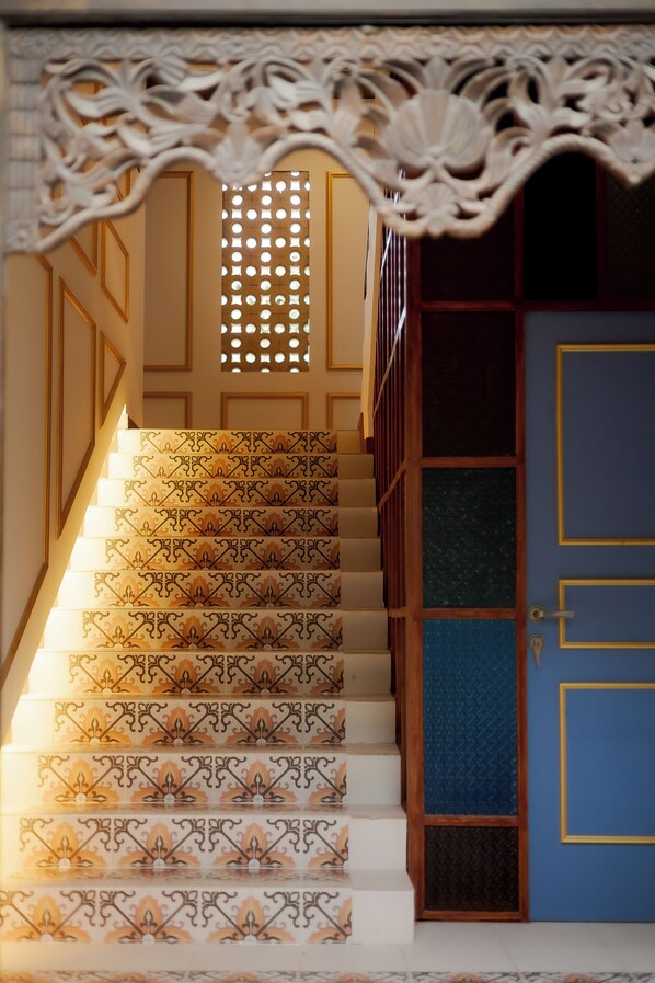 Eine Treppe mit aufwendiger Geländergestaltung und gemusterten Stufen, die zu einer Tür mit geometrischem Dekor führt.