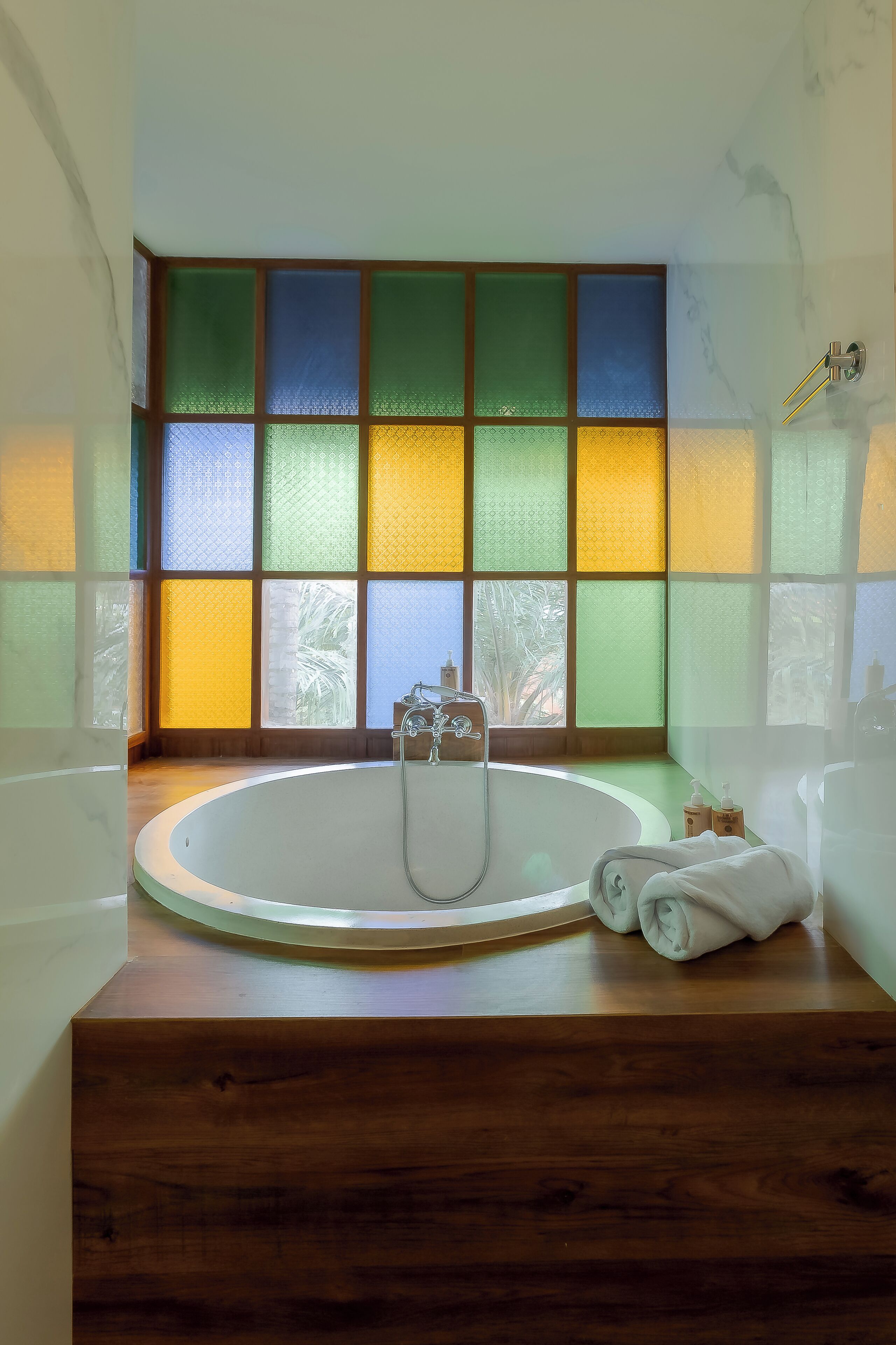 A bathroom with a bathtub, a wooden vanity, and a window with colorful glass panes.