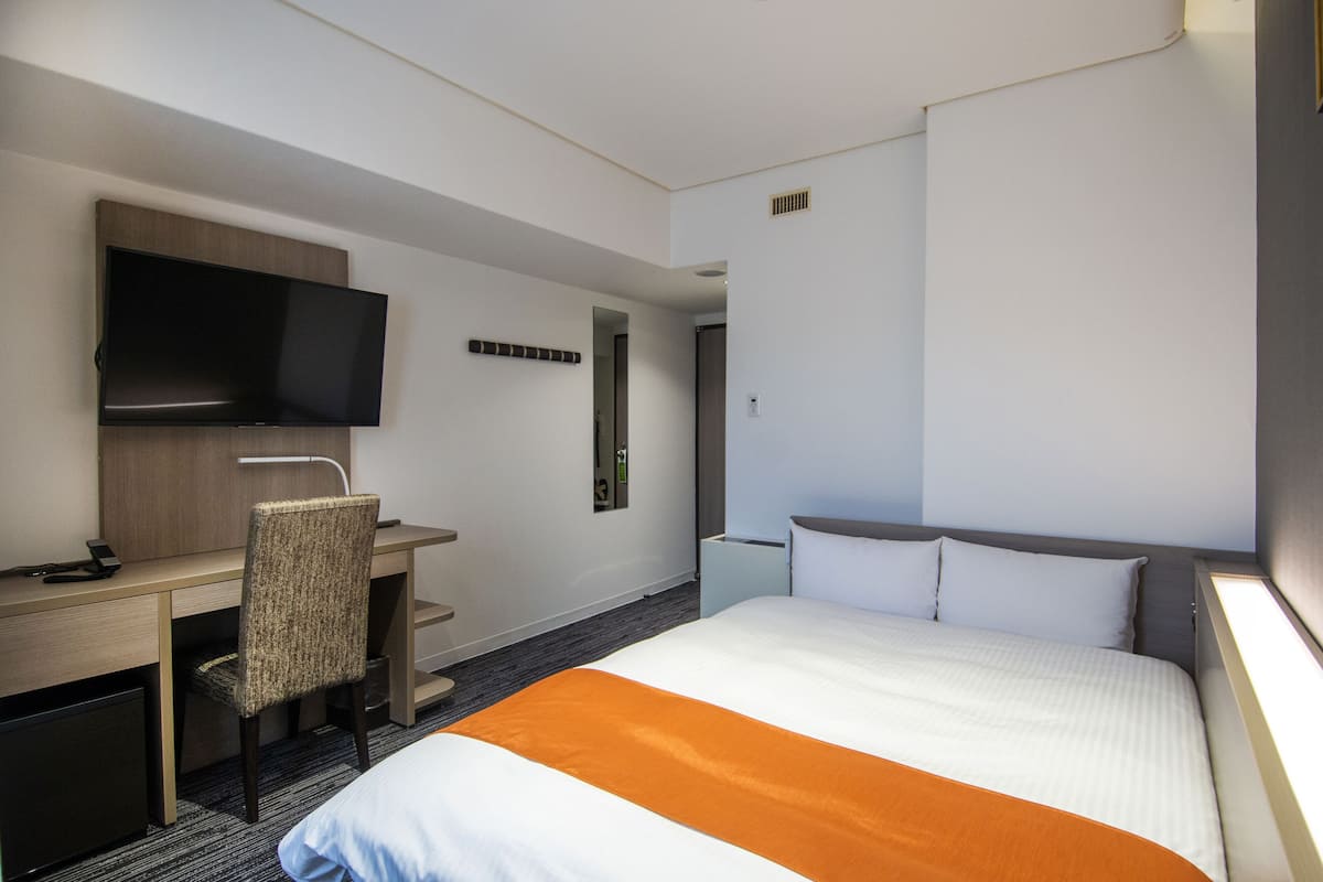 Een hotelkamer met een bed, een bureau met stoel, een televisie en een deur die naar een andere kamer leidt.