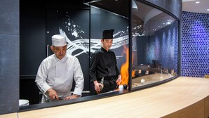 Two chefs in a modern kitchen with a reflective backsplash and a wooden countertop. - Niigata Daiichi Hotel (Niigata)