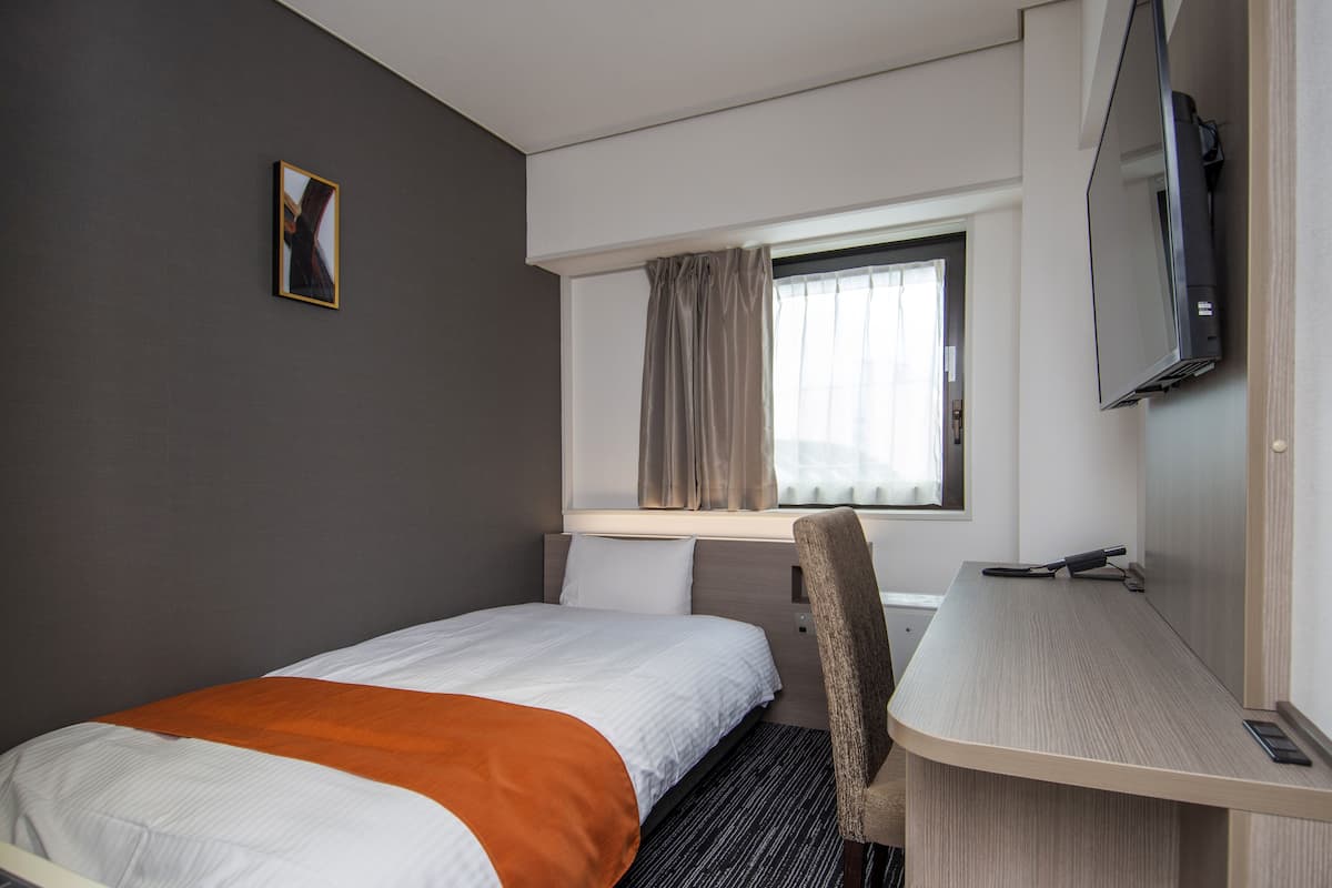 Een hotelkamer met een bed, een bureau, een stoel, een televisie en een raam met gordijnen.