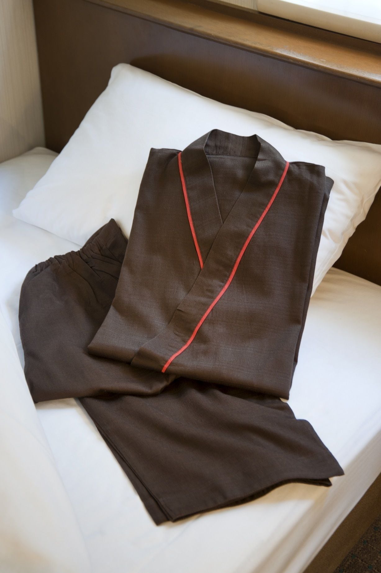 A neatly made bed with a white pillow and a brown garment folded on it.