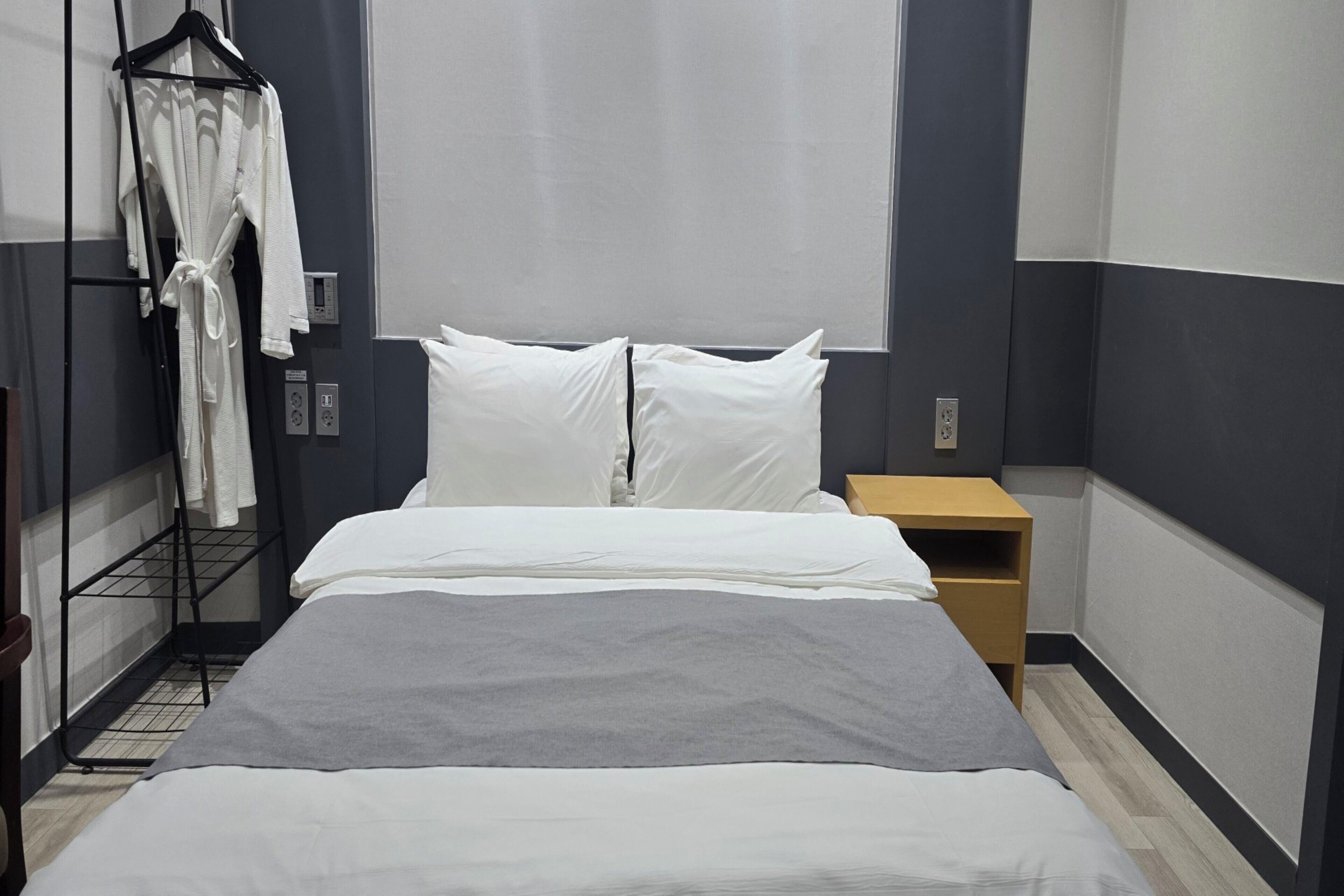 A hotel room with a bed, a nightstand, a robe hanging on a rack, and a window with curtains.