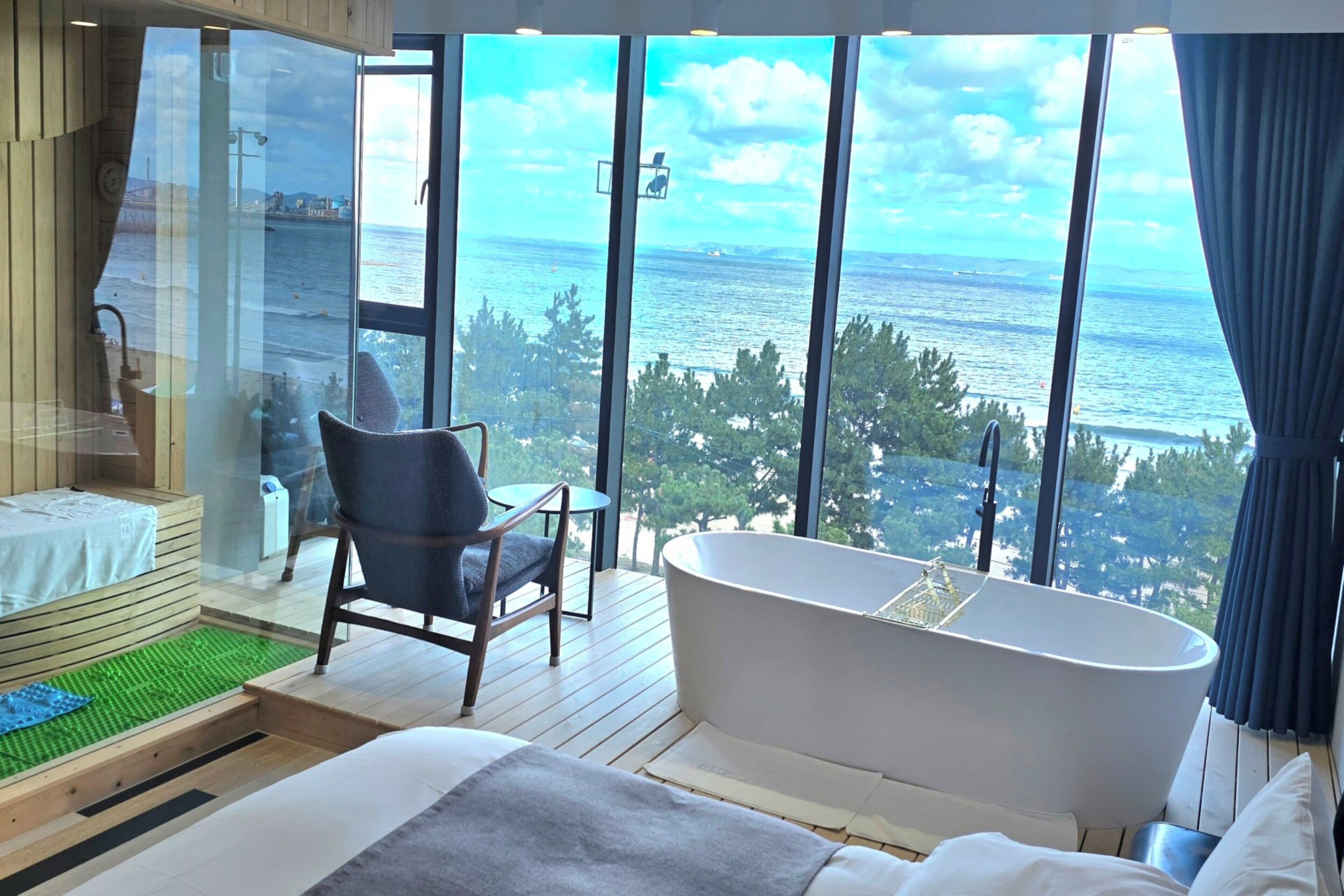 A modern bathroom with a large bathtub, a wooden bench, and a view of the sea.