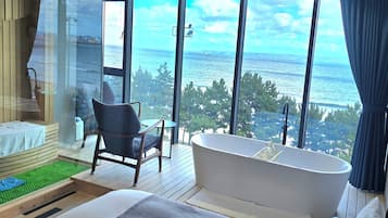 A modern bathroom with a large bathtub, a wooden bench, and a view of the sea.