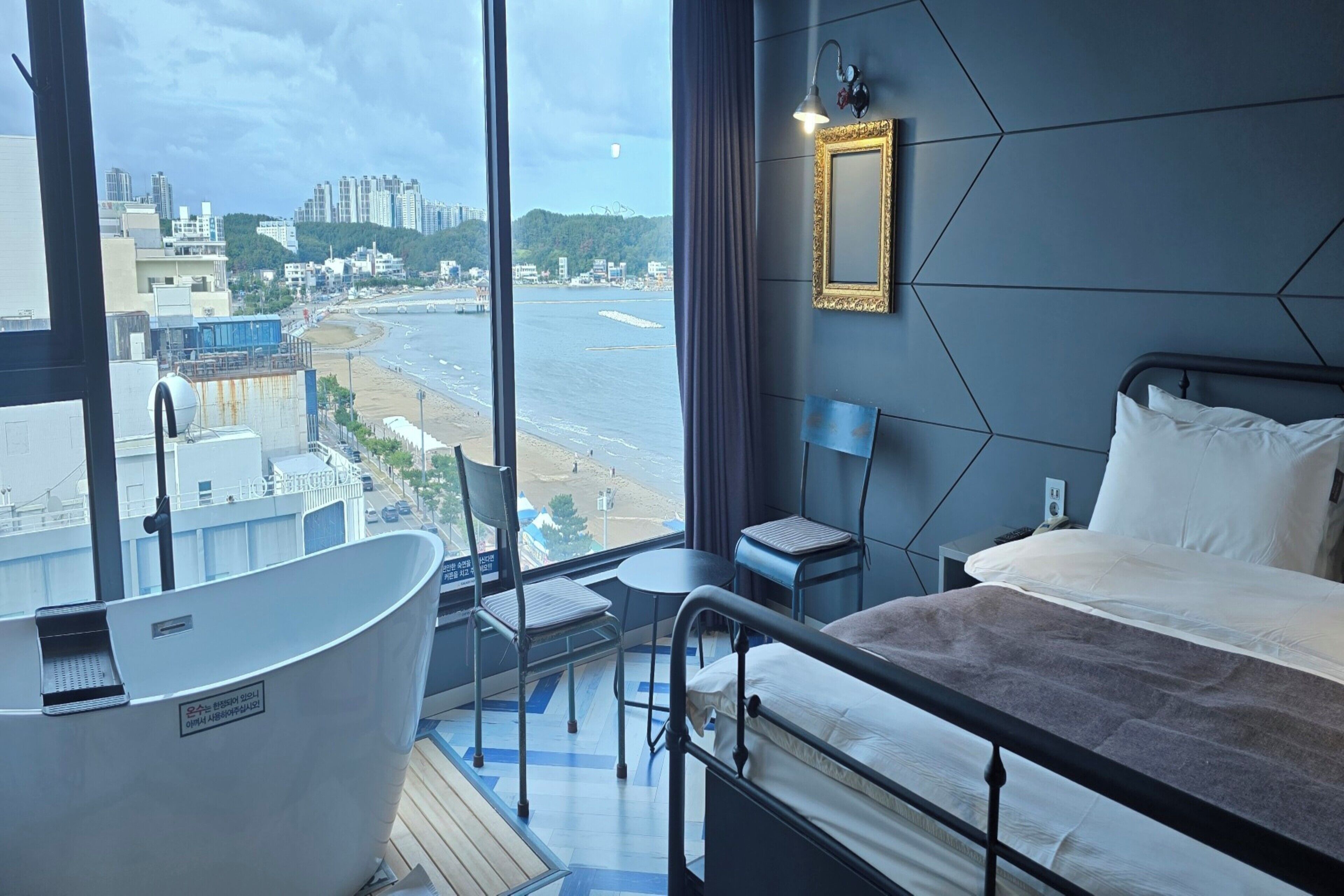 Una habitación de hotel moderna con un ventanal grande, una bañera, una cama y una pequeña mesa.