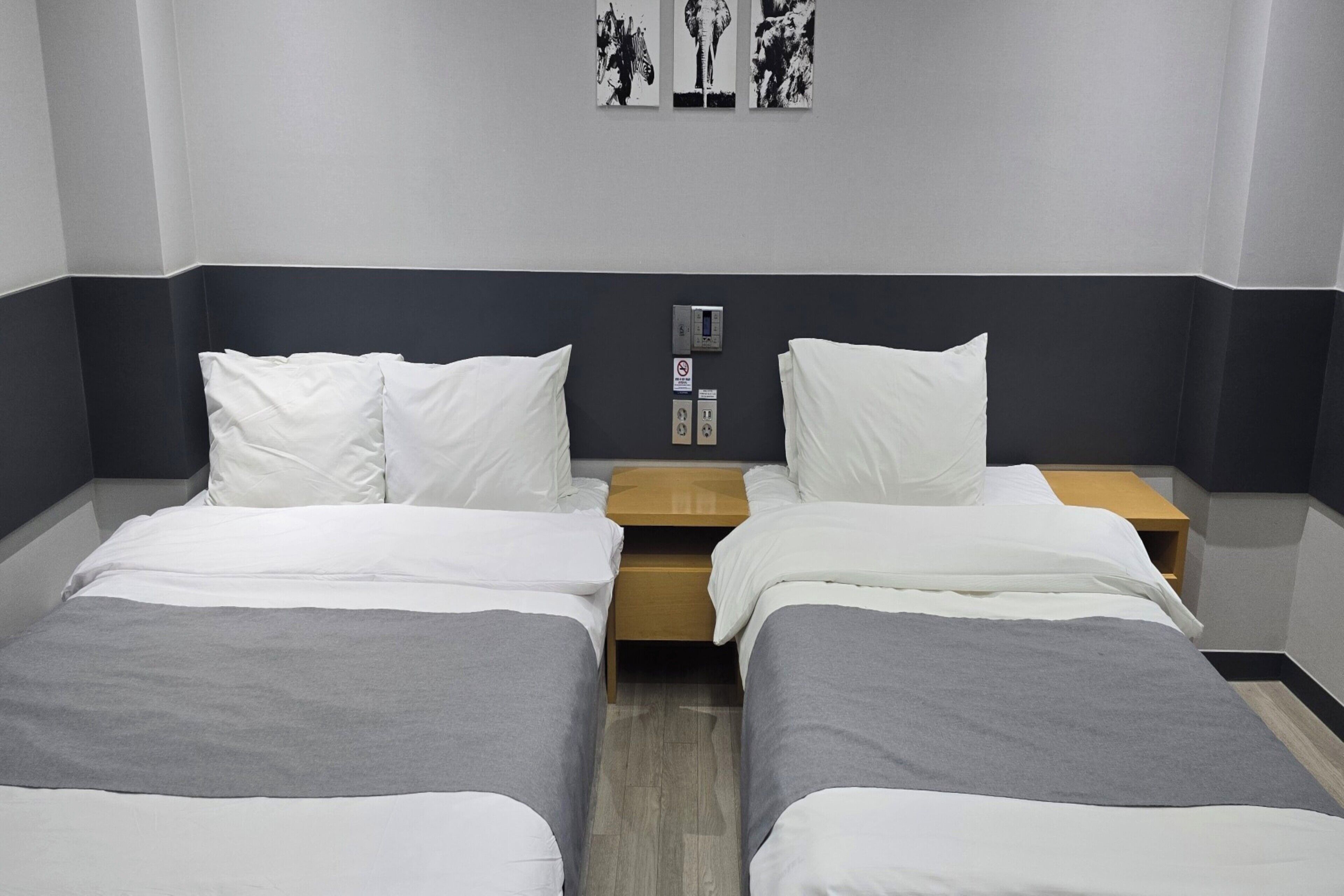 Habitación de hotel con dos camas, una mesita de noche y un panel de control en la pared.