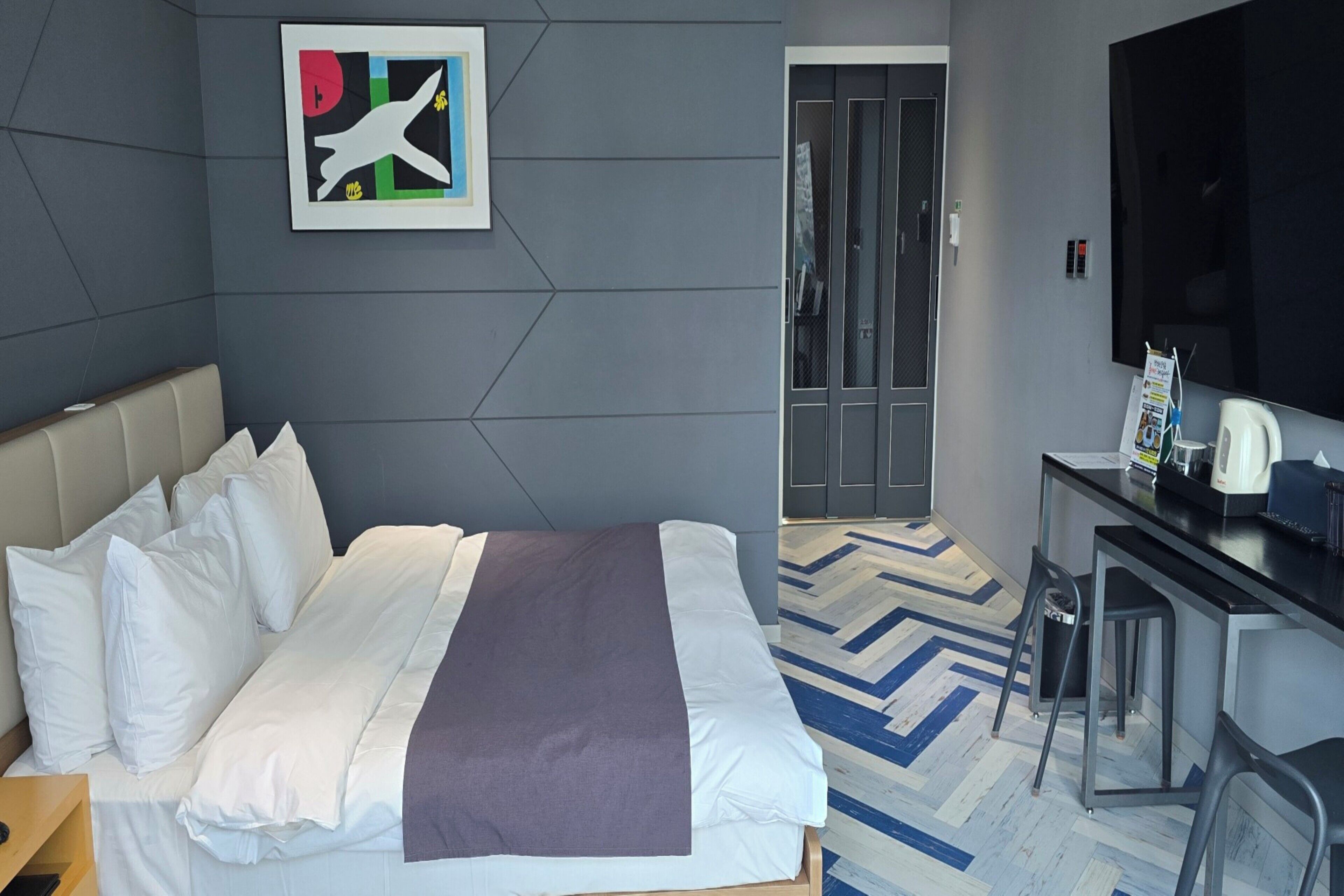 Una habitación de hotel con cama, escritorio, silla, televisor y puerta.