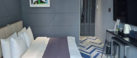 Una habitación de hotel con cama, escritorio, silla, televisor y puerta.