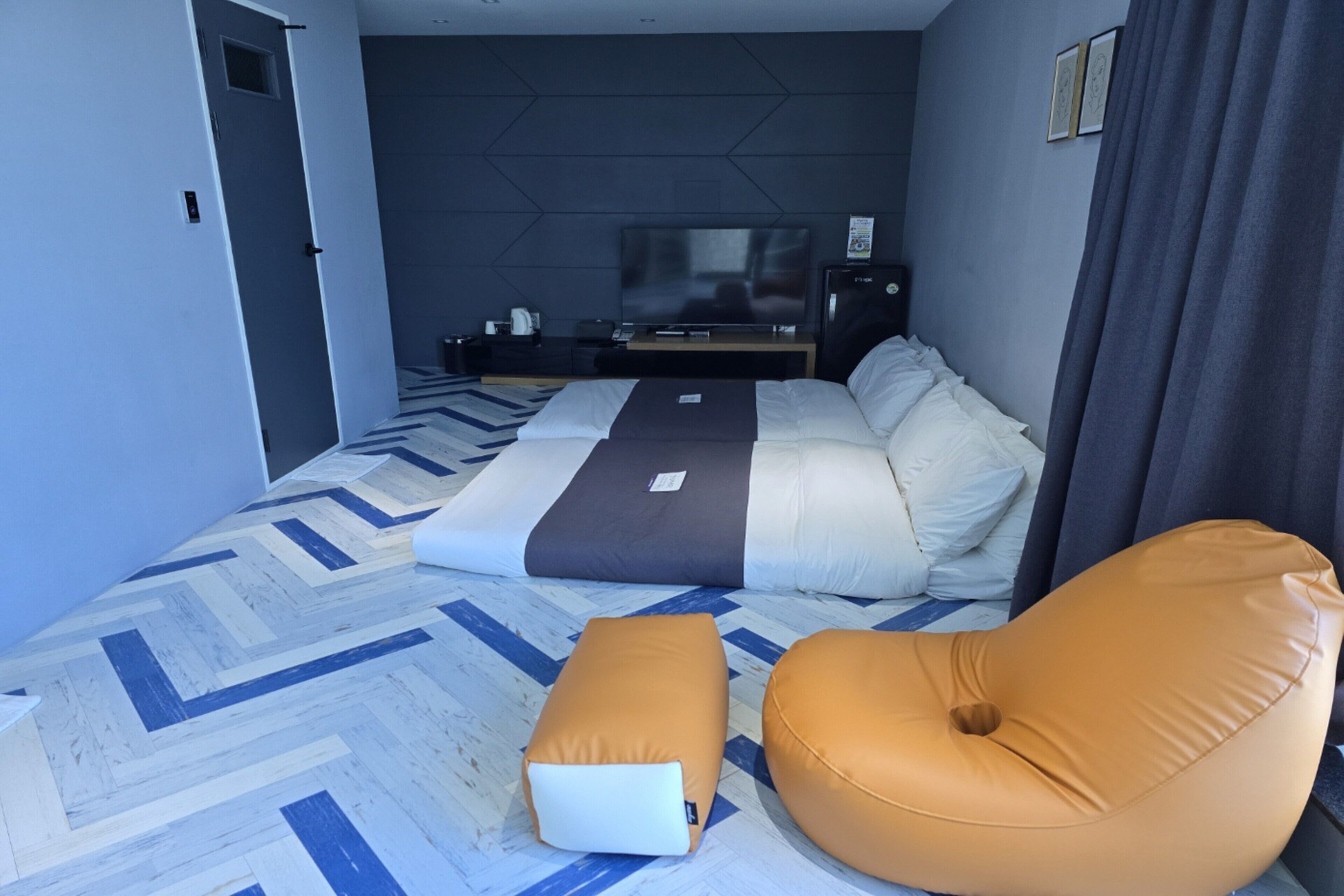 A modern hotel room with a large bed, a flat-screen TV, and a seating area with cushions.