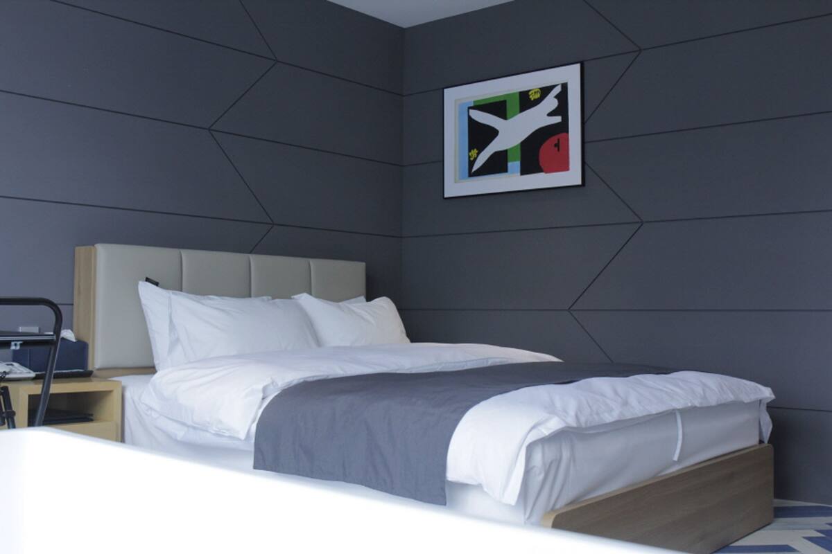 A modern hotel room with a bed, a headboard, a nightstand, and a wall-mounted artwork.