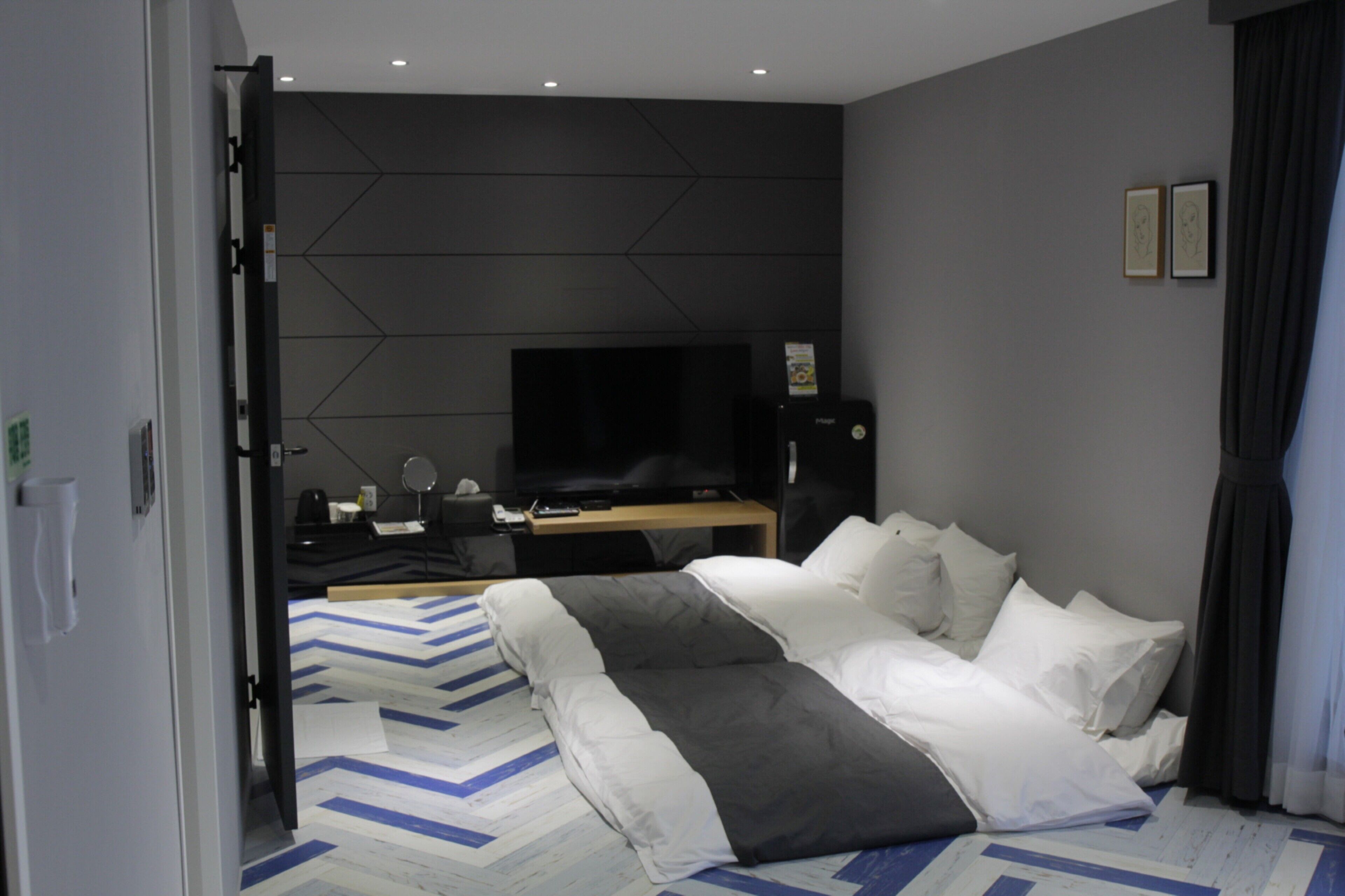 Ein modernes Hotelzimmer mit Bett, Flachbildfernseher, Schreibtisch mit Computer und Spiegel.