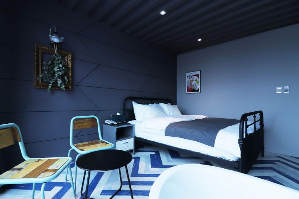 A modern bedroom with a bed, two chairs, a small table, and a nightstand.