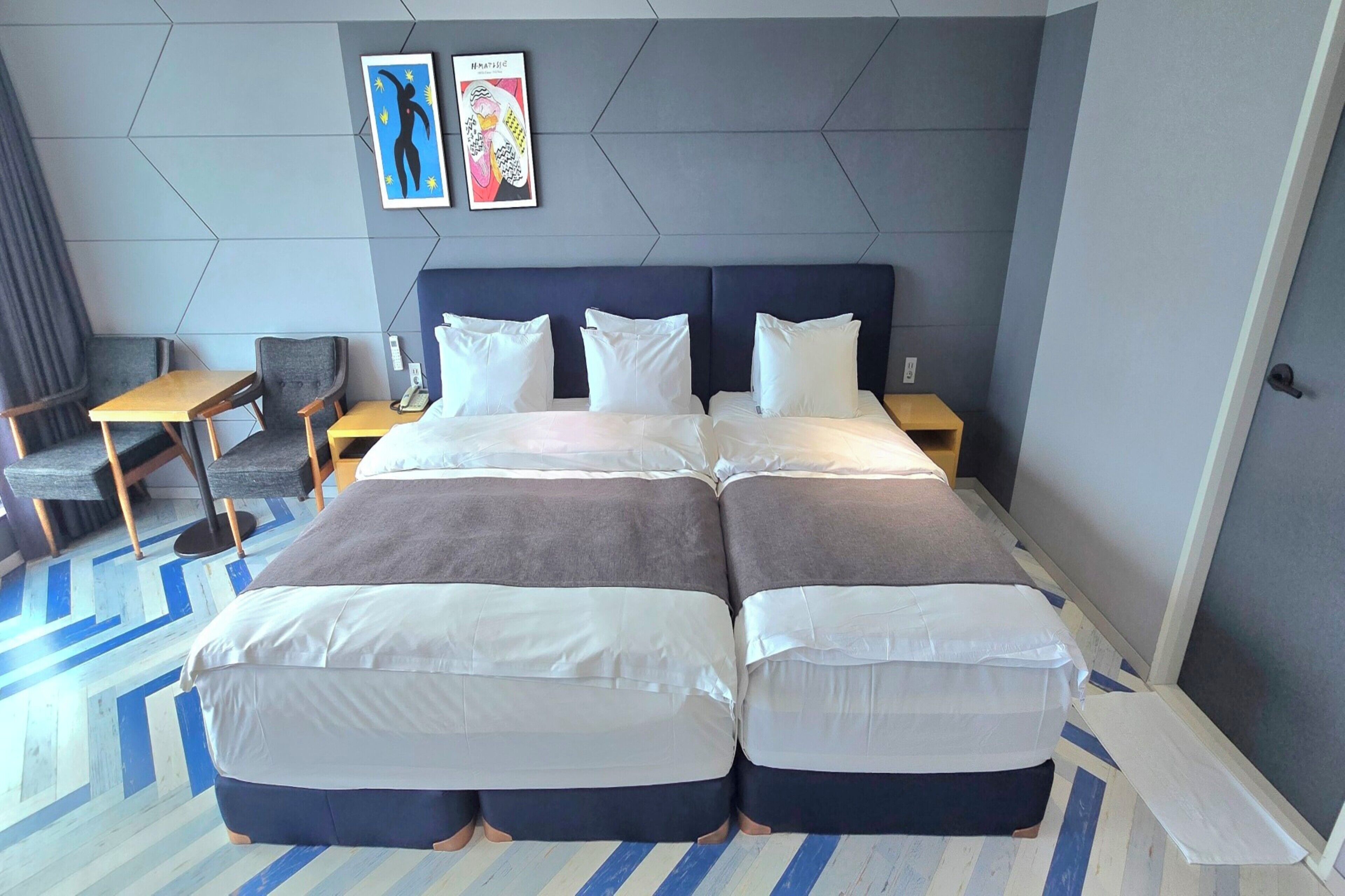 A hotel room with a large bed, two bedside tables, a desk, and a chair. There are two framed artworks on the wall.