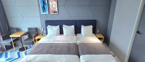 A hotel room with a large bed, two bedside tables, a desk, and a chair. There are two framed artworks on the wall.