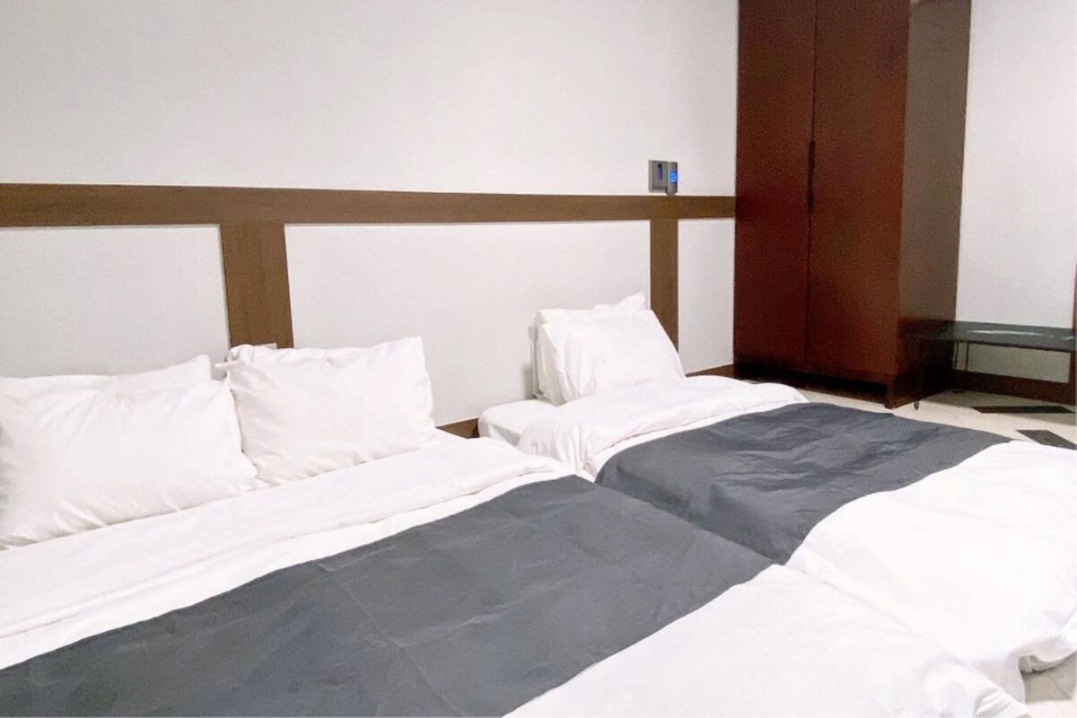 A hotel room with two beds, a wooden headboard, a small table, and a wardrobe.