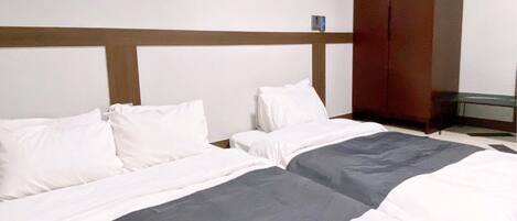 A hotel room with two beds, a wooden headboard, a small table, and a wardrobe.