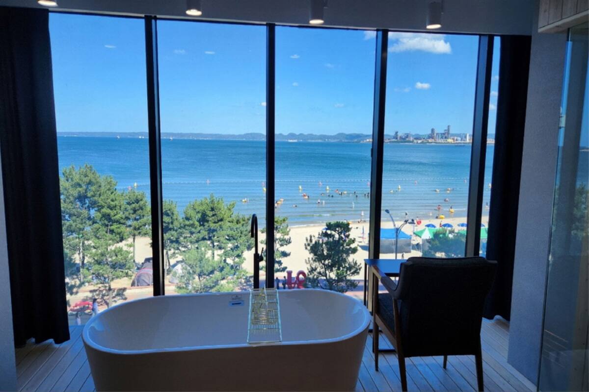 A room with a large bathtub and a view of the beach and sea.