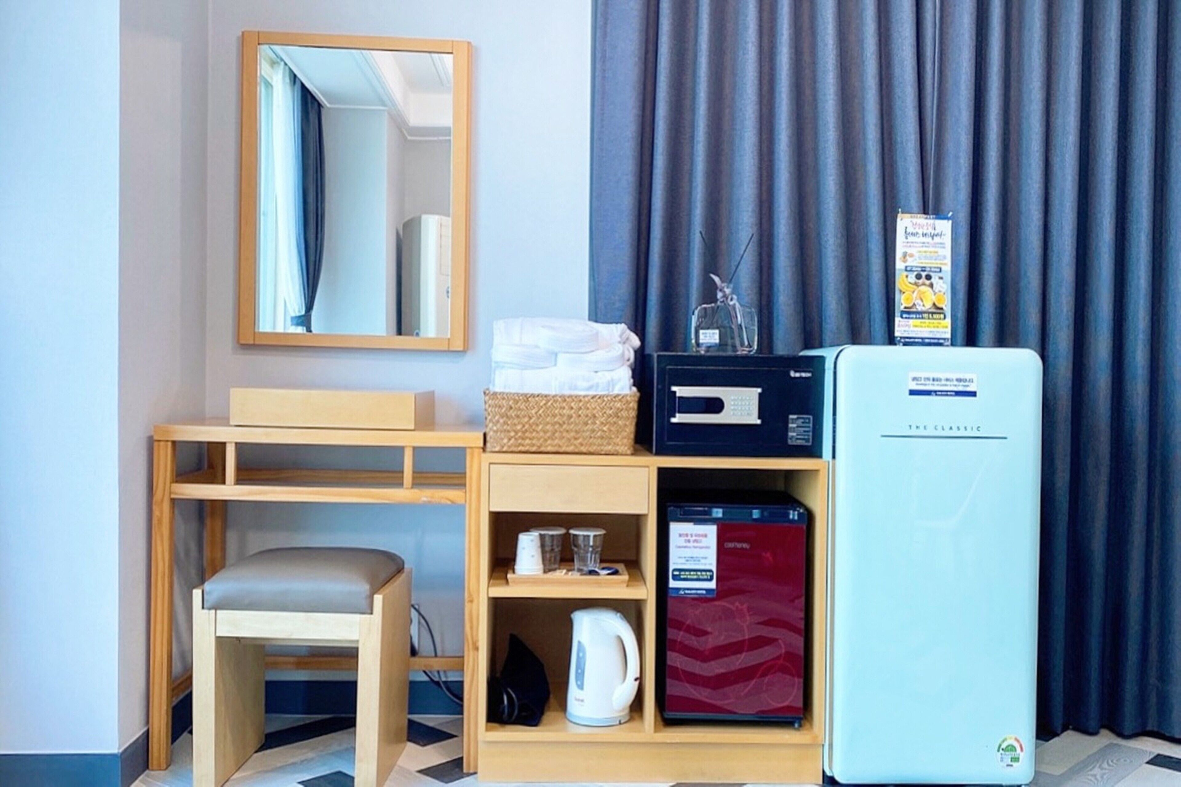 Une chambre d’hôtel comprenant un lit, un bureau avec une chaise, un four à micro-ondes, un réfrigérateur, un miroir et une fenêtre avec des rideaux.