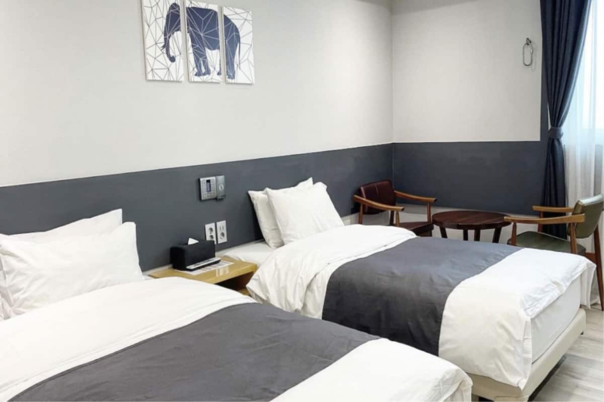 A hotel room with two beds, a desk, a chair, and a small table.