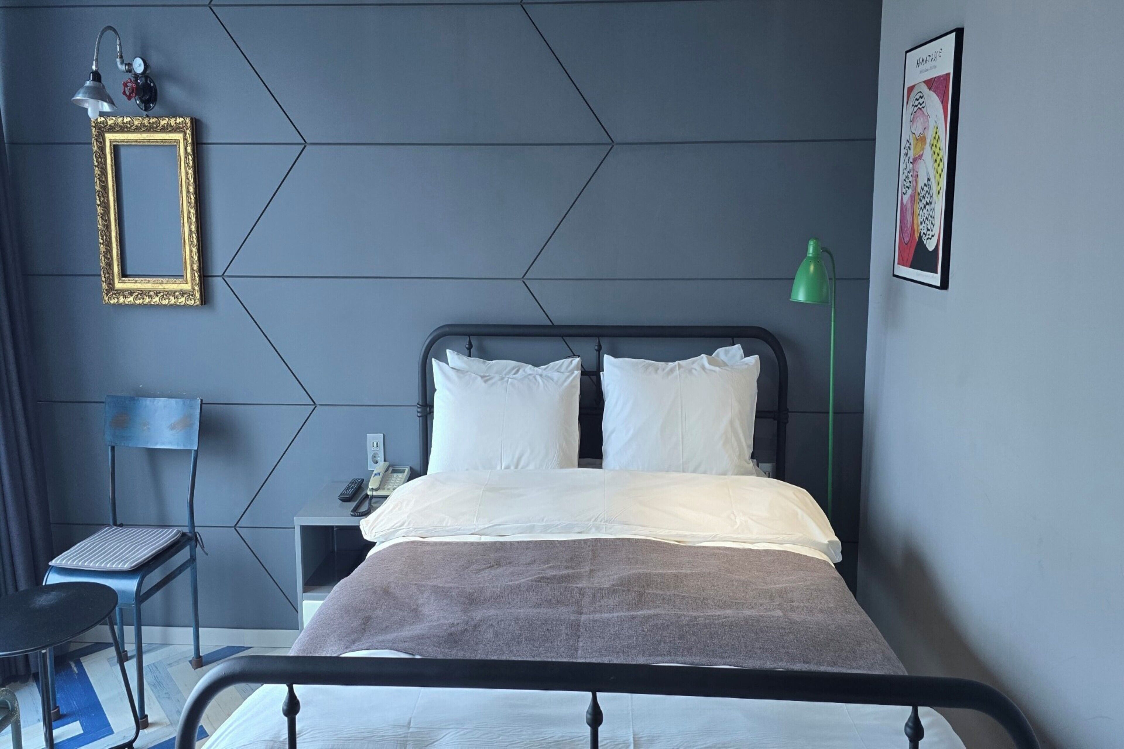 A modern bedroom with a bed, a nightstand, a desk, and a green desk lamp.