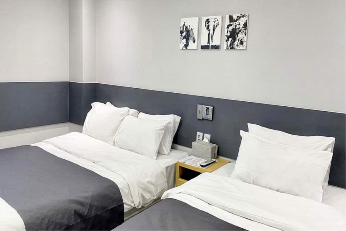 A hotel room with two beds, a bedside table with a lamp, and three black-and-white artwork pieces on the wall.