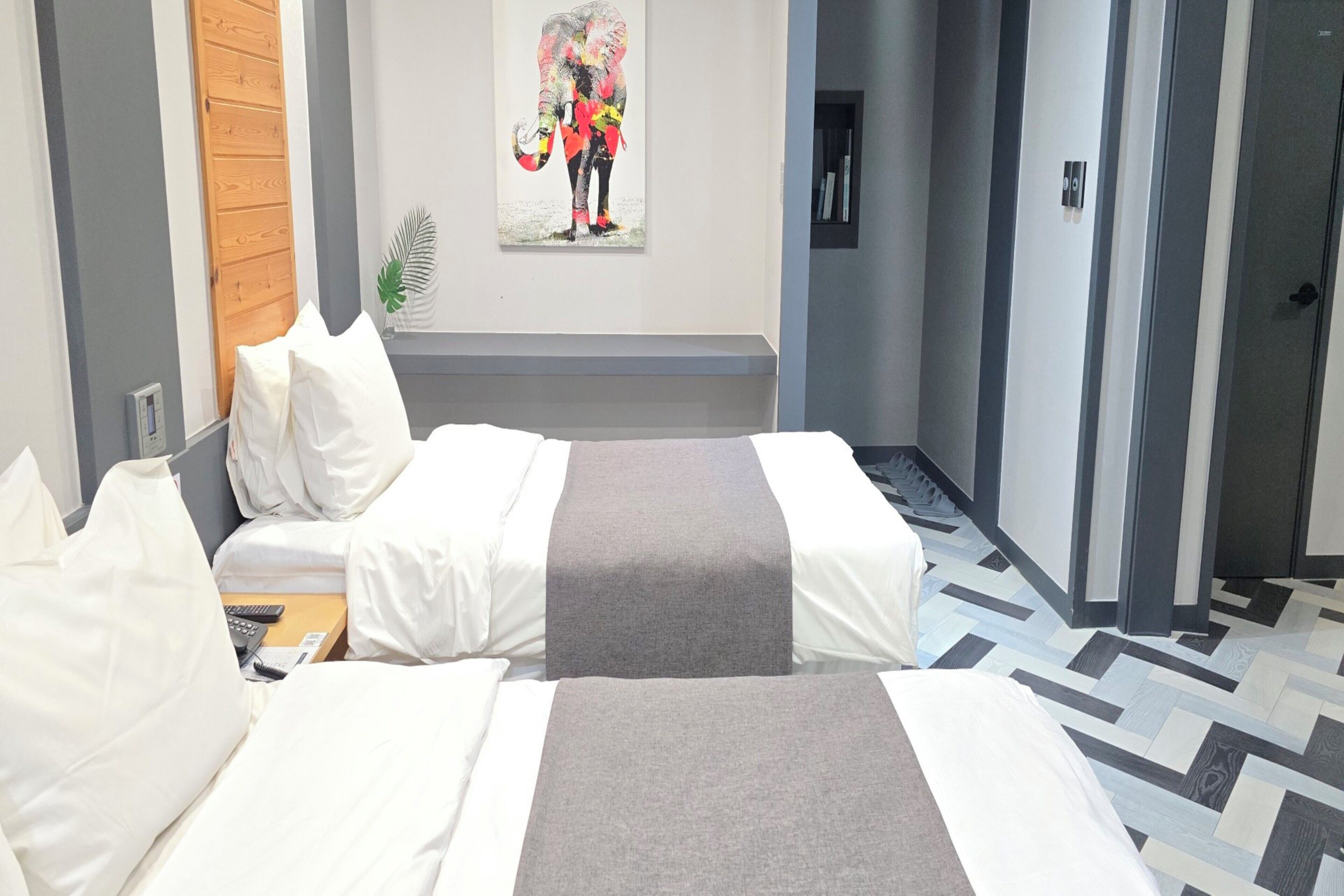 Une chambre d’hôtel avec deux lits, un banc, une plante et un tableau au mur.