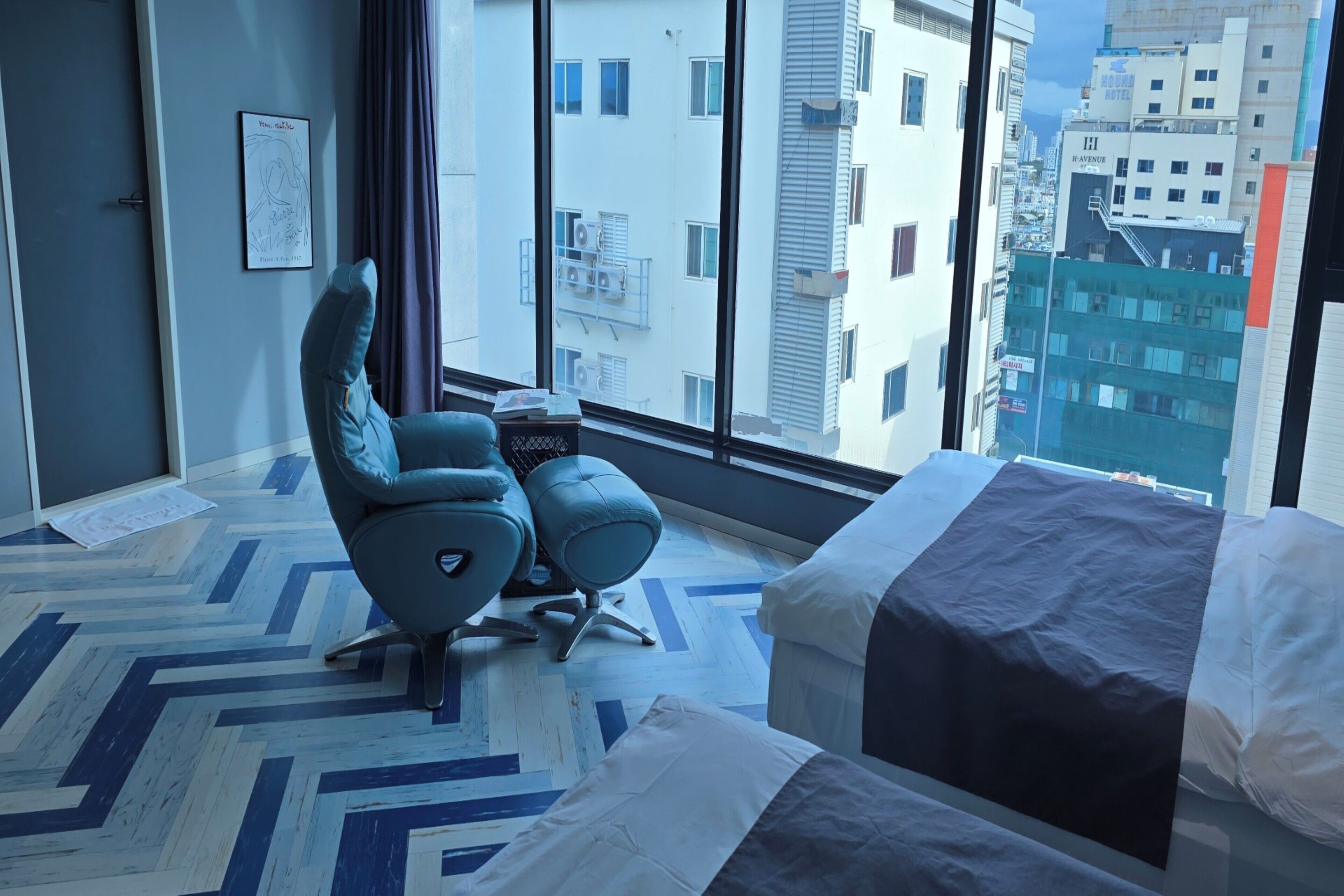 Une chambre d’hôtel moderne avec une grande fenêtre, un lit, une chaise et une petite table.