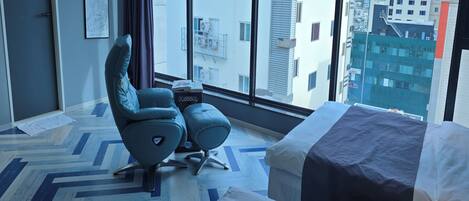 Une chambre d’hôtel moderne avec une grande fenêtre, un lit, une chaise et une petite table.