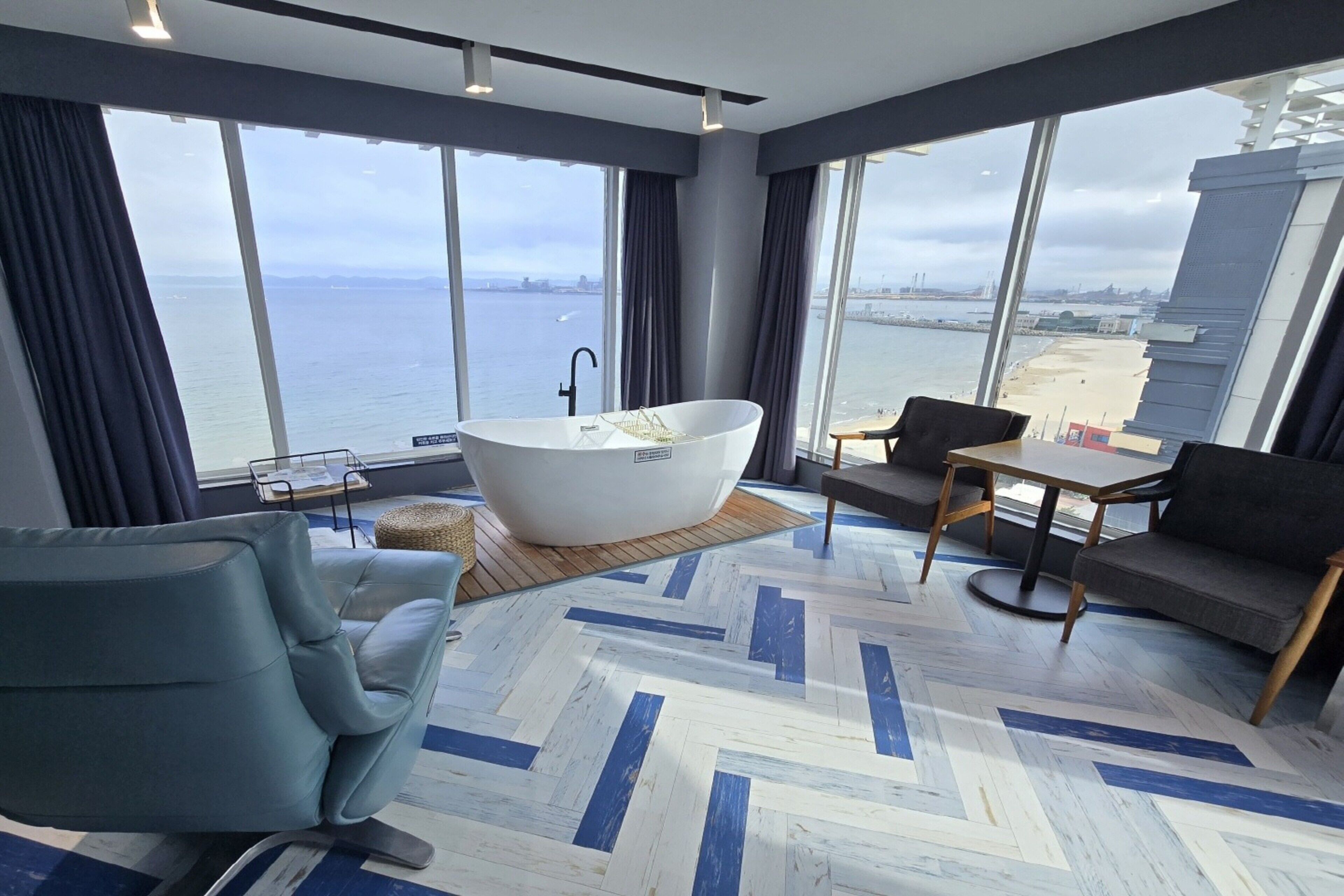 A modern room with a large window, a bathtub, a sofa, and a small table.