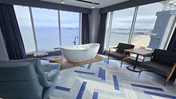 A modern room with a large window, a bathtub, a sofa, and a small table.