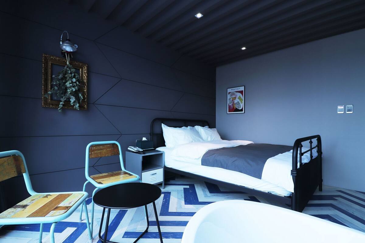 A modern hotel room with a bed, a desk, a chair, and a small table.