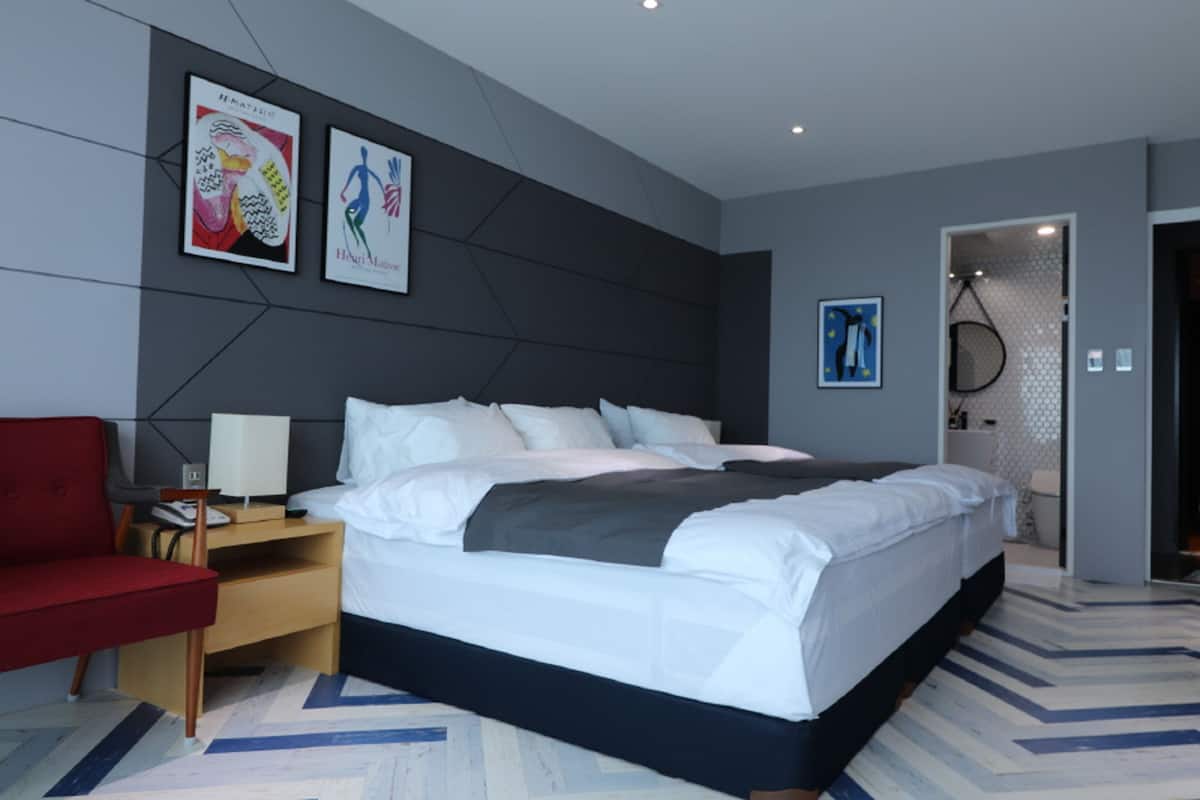 A modern hotel room with a large bed, a red armchair, and artwork on the walls.