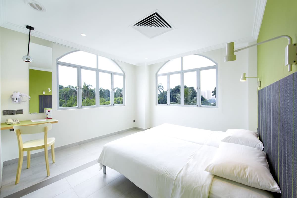 Une chambre d’hôtel moderne dotée d’un grand lit, d’un bureau et de deux grandes fenêtres donnant sur un paysage verdoyant.