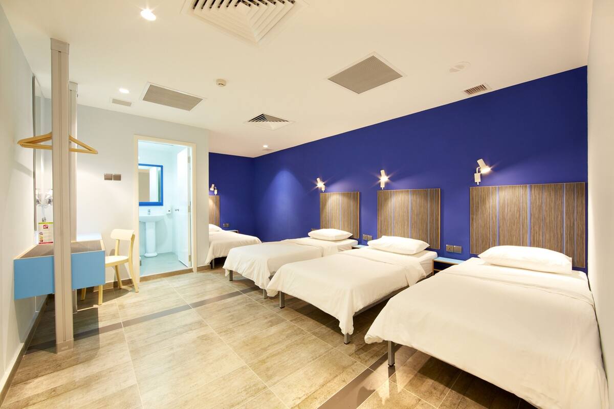 Une chambre d’hôtel avec quatre lits, une salle de bain et un bureau avec une chaise.