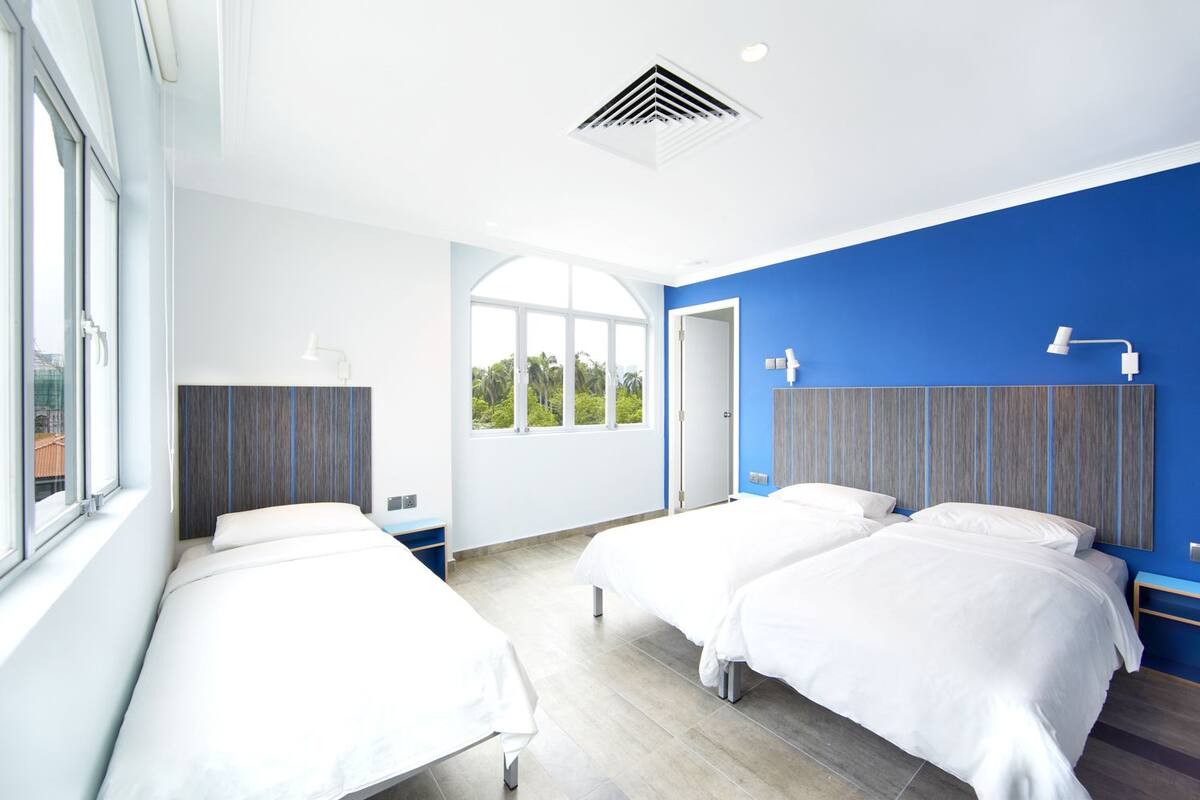 Une chambre d’hôtel moderne avec deux lits simples, une grande fenêtre et une vue sur la verdure.