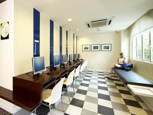 Un laboratorio de computadoras con filas de escritorios y sillas, piso a cuadros y una ventana que da a zonas verdes.