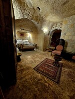 Una habitación rústica de piedra con una cama, una chimenea y una silla.
