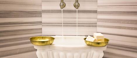 A marble-floored bathroom with a white pedestal sink, two brass faucets, and two gold bowls.