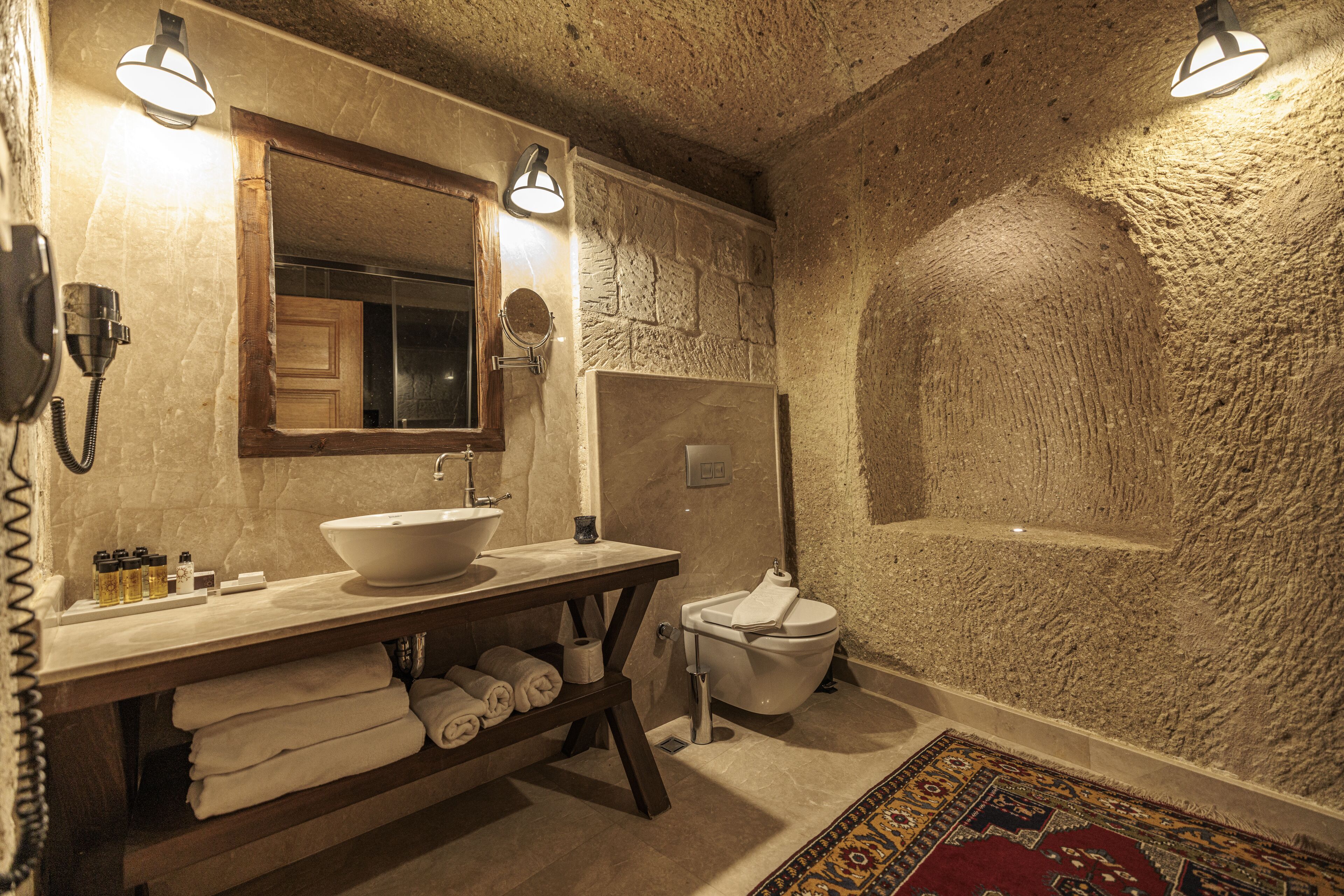 Bagno con parete in pietra, mobile bagno in legno, lavandino, WC e specchio.