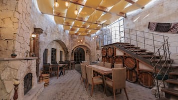 A rustic interior with stone walls, wooden furniture, and a staircase with barrels.