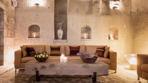 A cozy room with a sofa, a wooden coffee table, and a vase with flowers. There are candles on the table and a vase on the wall. - Exedra Cappadocia ( Ürgüp)