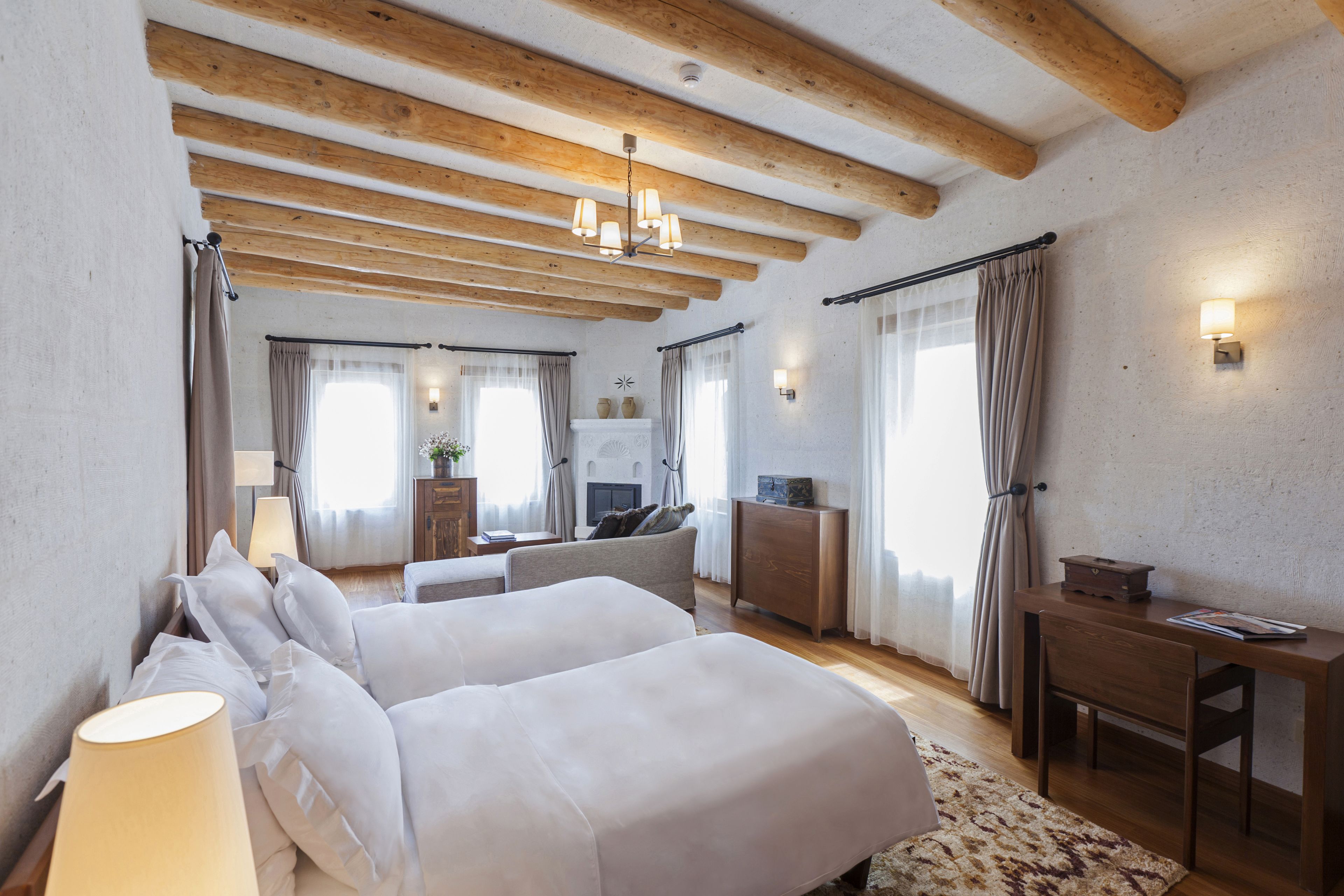 Een moderne hotelkamer met twee bedden, houten balken, een bureau en een open haard.