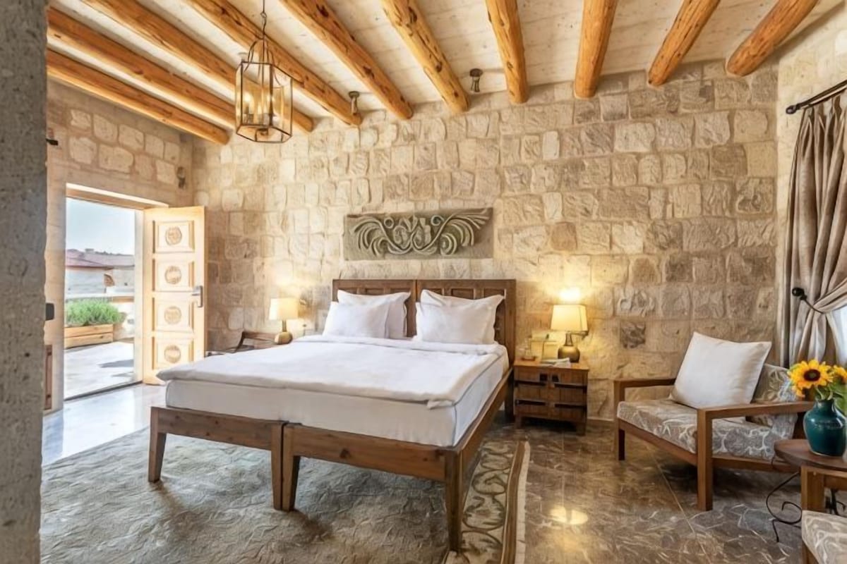 A bedroom with a stone wall, wooden bed frame, bedside tables, and a view through an open door.
