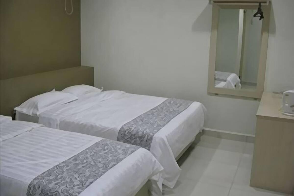 Ein Hotelzimmer mit zwei Betten, einem kleinen Nachttisch, einem Spiegel und einer schlichten Wand.